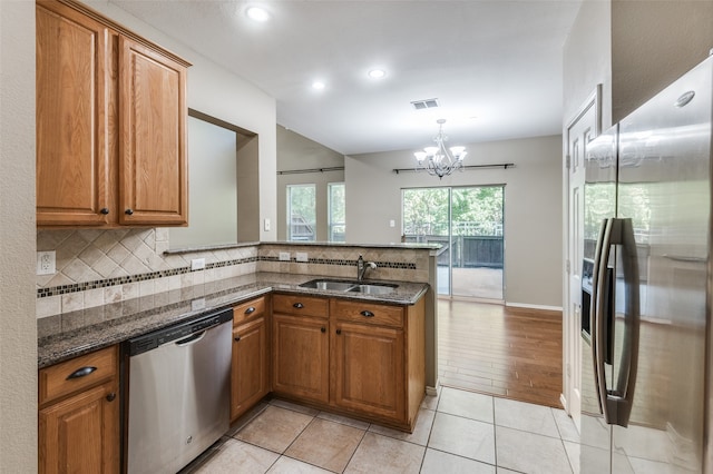 kitchen featuring kitchen peninsula, appliances with stainless steel finishes, dark stone countertops, a notable chandelier, and sink