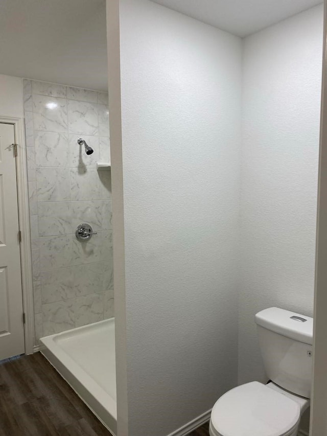 bathroom featuring toilet, hardwood / wood-style flooring, and tiled shower