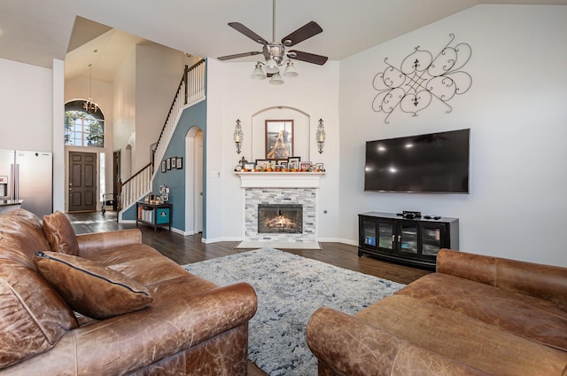 living room featuring dark hardwood / wood-style flooring, high vaulted ceiling, a stone fireplace, and ceiling fan