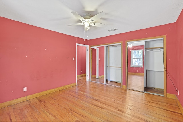 unfurnished bedroom featuring ceiling fan, light wood-type flooring, and two closets