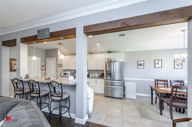 kitchen with light tile patterned floors, stainless steel fridge with ice dispenser, white cabinetry, light stone countertops, and pendant lighting