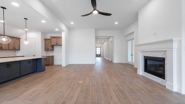 unfurnished living room featuring ceiling fan, recessed lighting, a premium fireplace, baseboards, and light wood finished floors