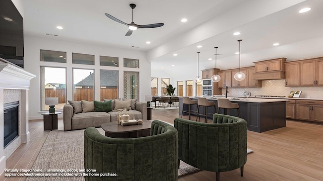 living area featuring light wood-style floors, recessed lighting, ceiling fan, and a tiled fireplace