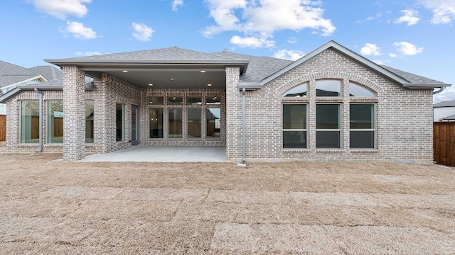 back of house featuring brick siding, a patio, fence, and roof with shingles