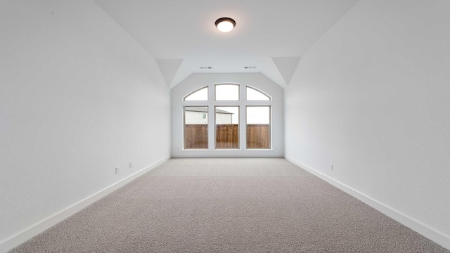 spare room featuring light carpet, baseboards, and lofted ceiling