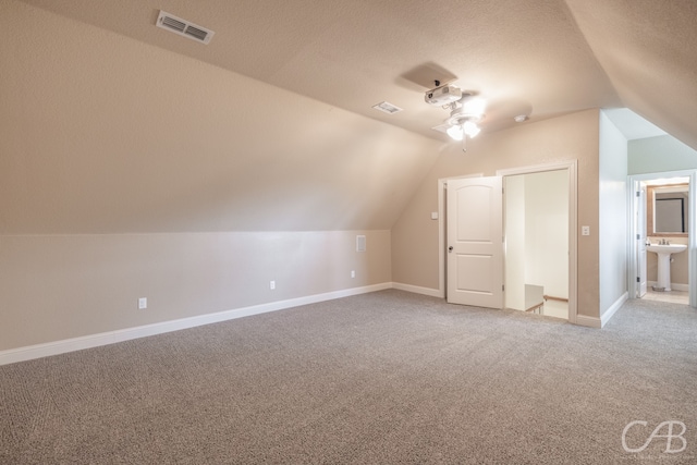 bonus room with sink, a textured ceiling, carpet, and lofted ceiling