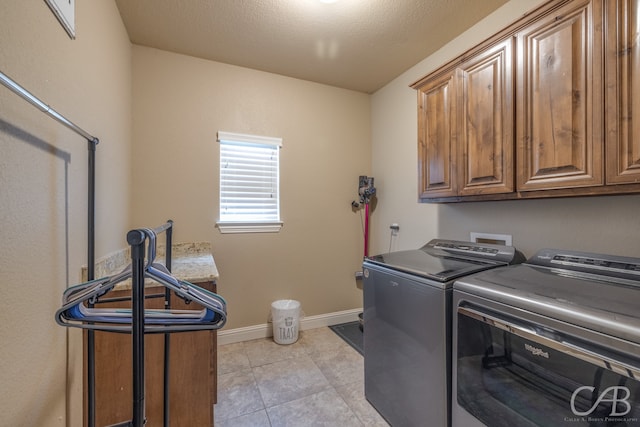 washroom with cabinets, a textured ceiling, washing machine and dryer, and light tile patterned floors