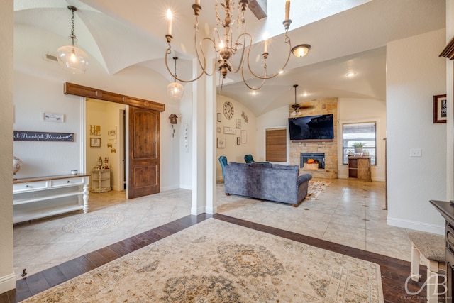 living room with a notable chandelier, hardwood / wood-style floors, vaulted ceiling, and a stone fireplace