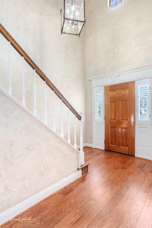 foyer entrance featuring an inviting chandelier, hardwood / wood-style flooring, and a towering ceiling