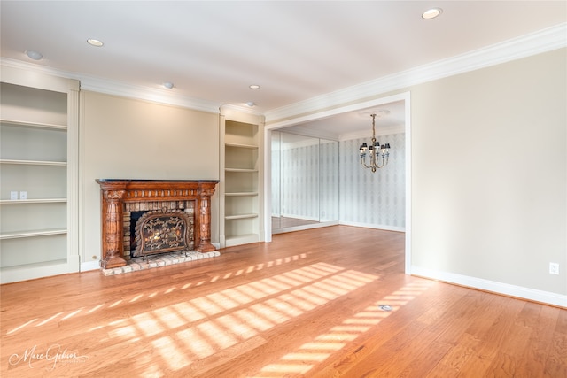 unfurnished living room with crown molding, wood-type flooring, built in features, a notable chandelier, and a fireplace