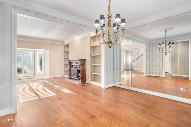 unfurnished living room with a brick fireplace, built in shelves, crown molding, wood-type flooring, and a chandelier