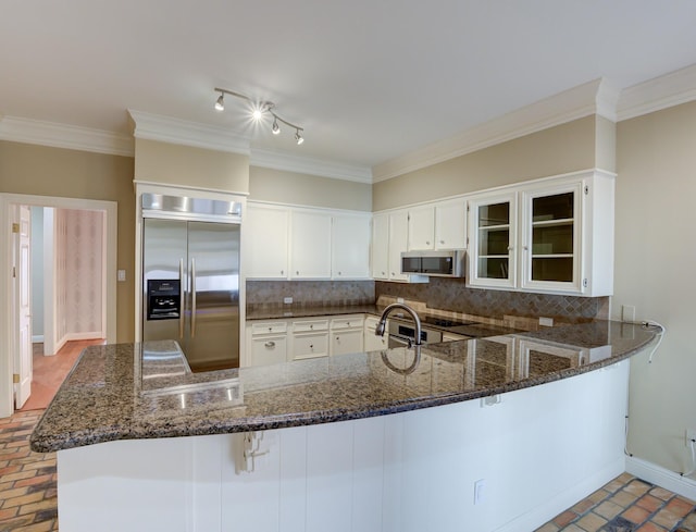 kitchen featuring stainless steel appliances, dark stone counters, brick floor, and backsplash