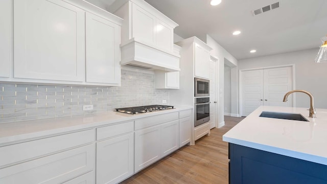 kitchen with light wood finished floors, decorative backsplash, appliances with stainless steel finishes, white cabinets, and a sink