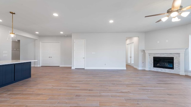 unfurnished living room featuring light wood-style flooring, a glass covered fireplace, a ceiling fan, and recessed lighting