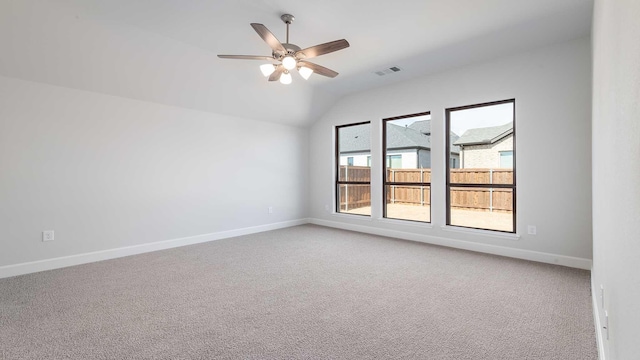 spare room featuring light colored carpet, visible vents, a ceiling fan, vaulted ceiling, and baseboards