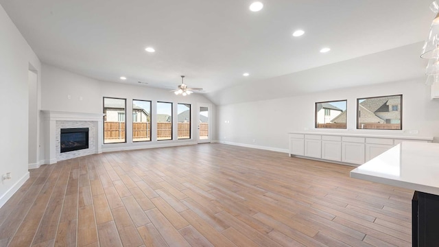 unfurnished living room with lofted ceiling, recessed lighting, baseboards, light wood-style floors, and a glass covered fireplace