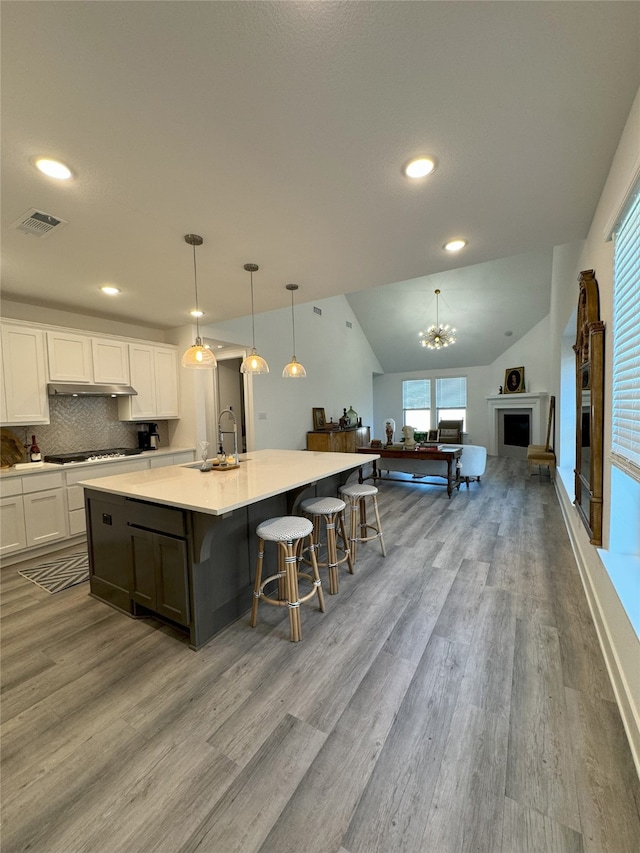 kitchen featuring a large island, white cabinets, hanging light fixtures, vaulted ceiling, and light hardwood / wood-style flooring