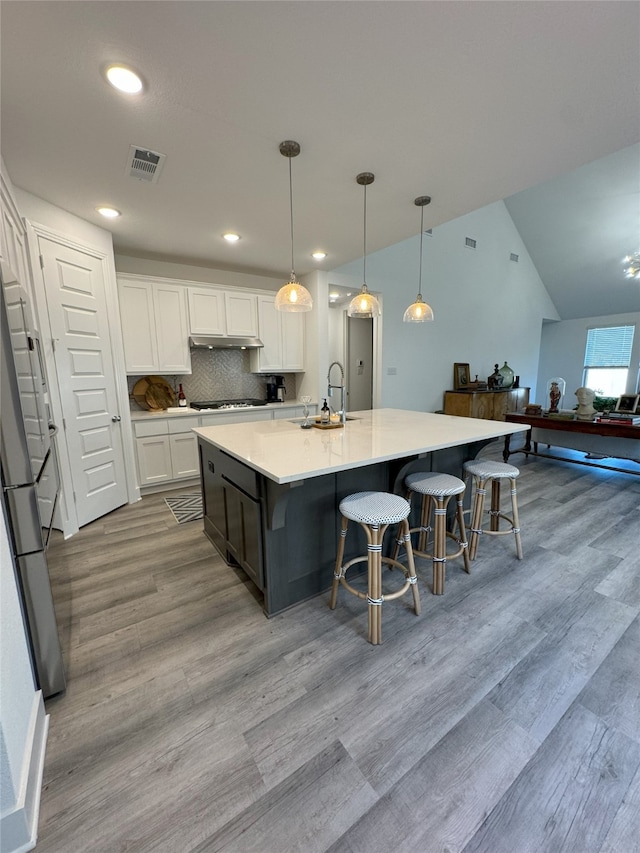 kitchen with lofted ceiling, white cabinets, an island with sink, light hardwood / wood-style flooring, and decorative light fixtures