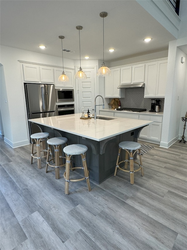 kitchen with white cabinets, hanging light fixtures, sink, light hardwood / wood-style floors, and stainless steel appliances