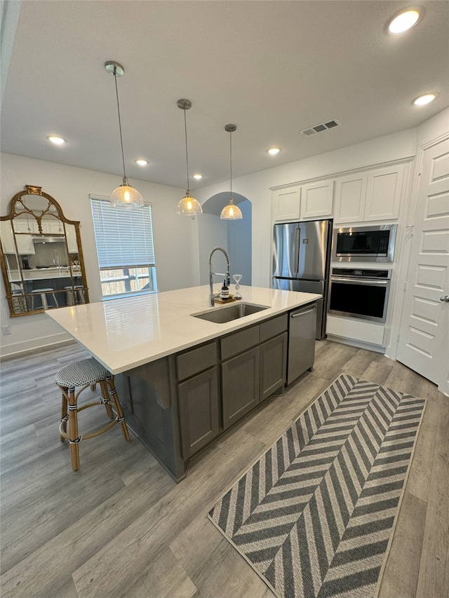 kitchen featuring appliances with stainless steel finishes, sink, light wood-type flooring, pendant lighting, and white cabinets