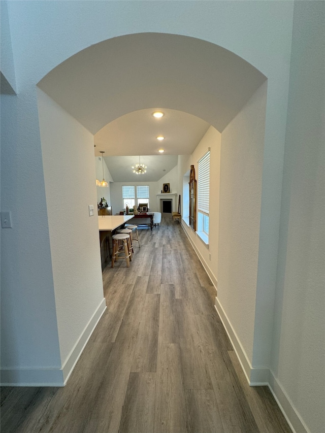 hallway featuring hardwood / wood-style flooring, lofted ceiling, and a chandelier