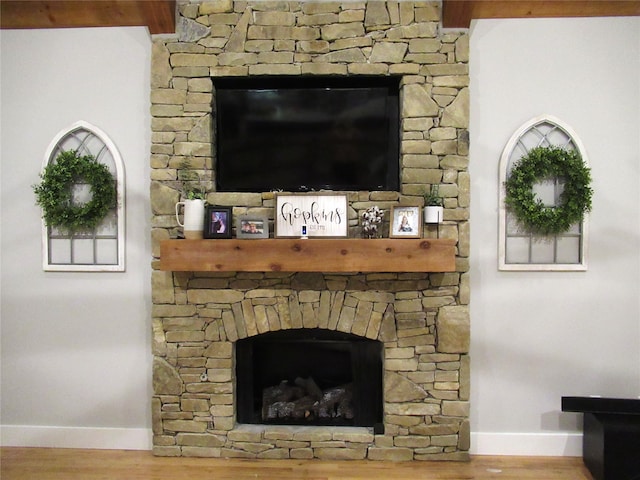 room details featuring beam ceiling, hardwood / wood-style floors, and a stone fireplace