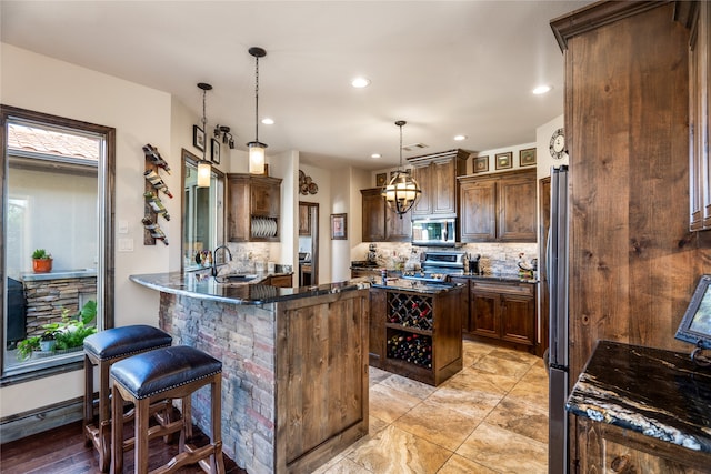 kitchen with stainless steel appliances, dark brown cabinetry, decorative backsplash, decorative light fixtures, and kitchen peninsula