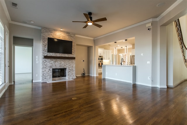 unfurnished living room featuring a stone fireplace, dark hardwood / wood-style floors, ornamental molding, sink, and ceiling fan