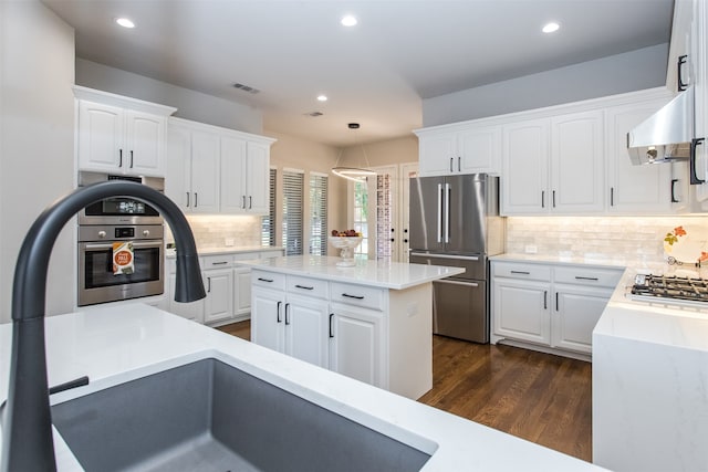 kitchen featuring appliances with stainless steel finishes, hanging light fixtures, white cabinetry, dark wood-type flooring, and extractor fan