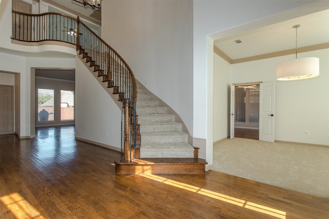 stairs with ornamental molding, a high ceiling, and wood-type flooring