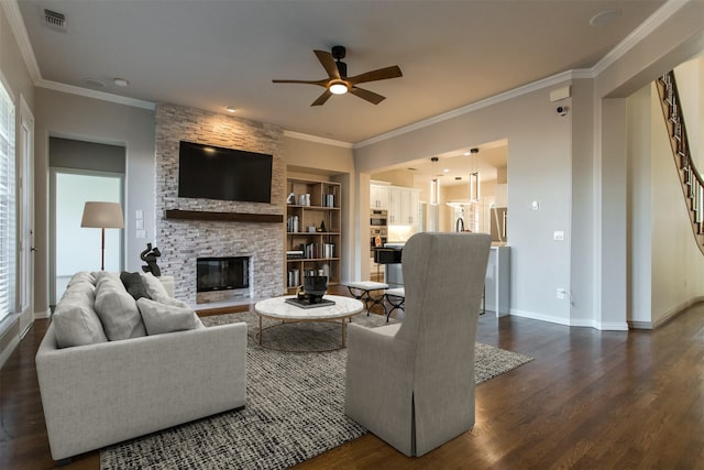 living room with a stone fireplace, built in features, ceiling fan, crown molding, and dark hardwood / wood-style floors