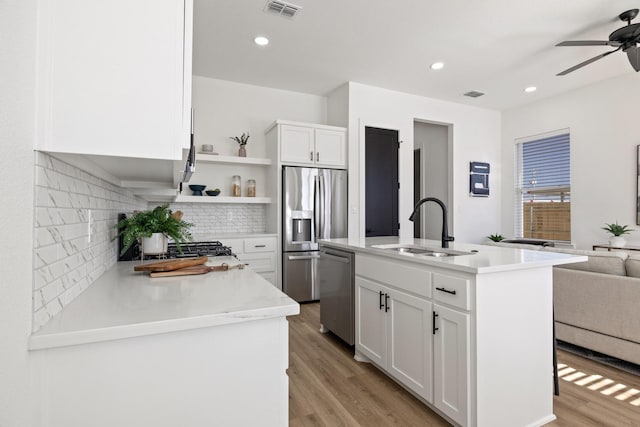 kitchen with appliances with stainless steel finishes, sink, white cabinets, a kitchen island with sink, and light wood-type flooring