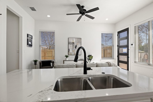 kitchen with light stone counters, sink, and ceiling fan