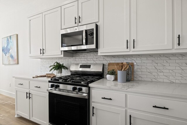 kitchen with white cabinetry, backsplash, light stone countertops, and appliances with stainless steel finishes