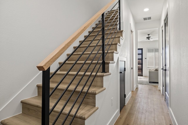 staircase featuring wood-type flooring and ceiling fan