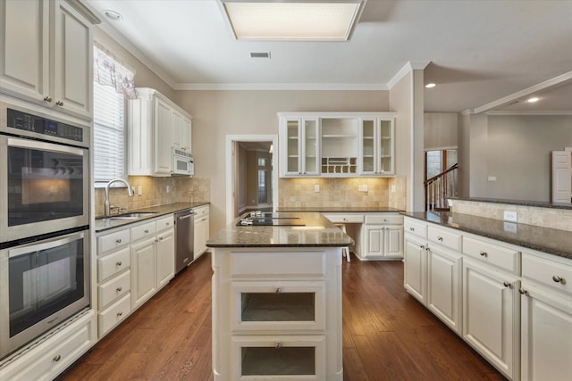 kitchen featuring stainless steel appliances, dark stone counters, a kitchen island, white cabinets, and sink