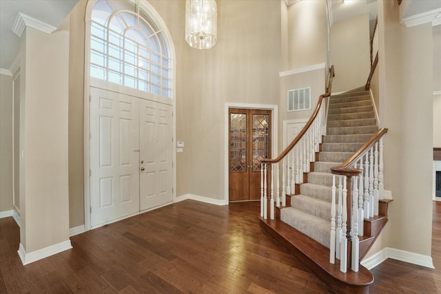 entryway with ornamental molding, a towering ceiling, dark hardwood / wood-style floors, and a notable chandelier