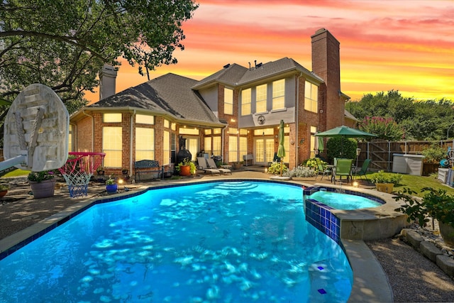 pool at dusk with an in ground hot tub and a patio