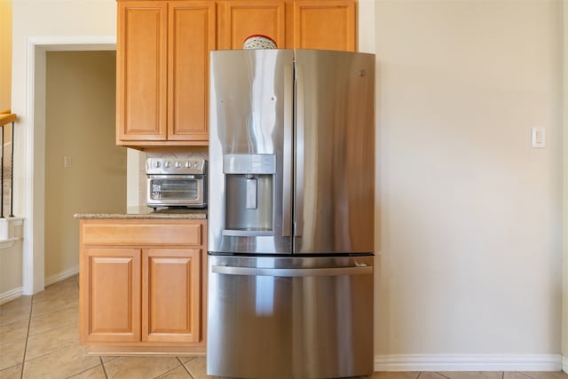 kitchen featuring stainless steel fridge, light stone countertops, and light tile patterned flooring