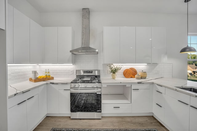 kitchen featuring backsplash, stainless steel range with gas stovetop, white cabinetry, wall chimney exhaust hood, and decorative light fixtures