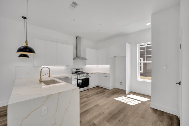 kitchen featuring wall chimney range hood, hanging light fixtures, white cabinetry, gas range, and light hardwood / wood-style flooring