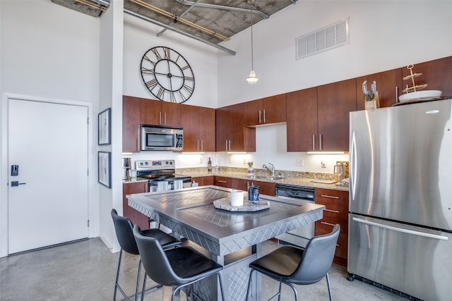 kitchen featuring sink, a kitchen bar, stainless steel appliances, a high ceiling, and pendant lighting