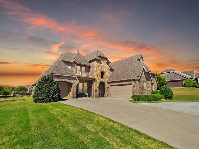 french country style house with driveway, a front lawn, stone siding, a garage, and brick siding