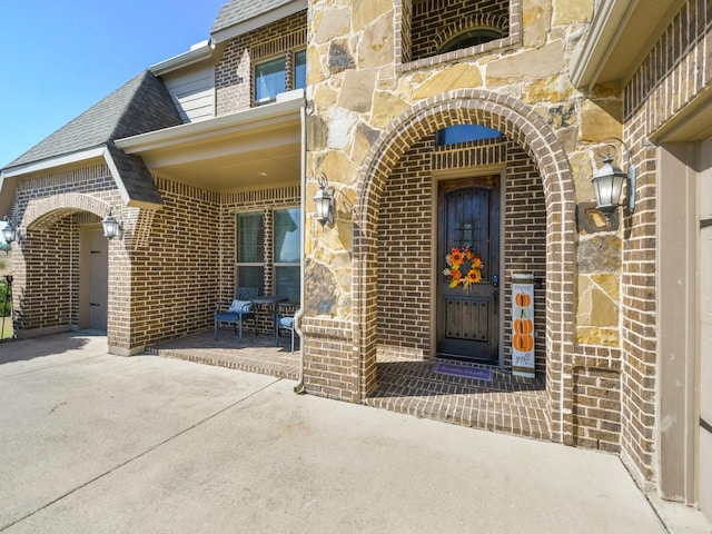 view of exterior entry with concrete driveway, brick siding, and a shingled roof