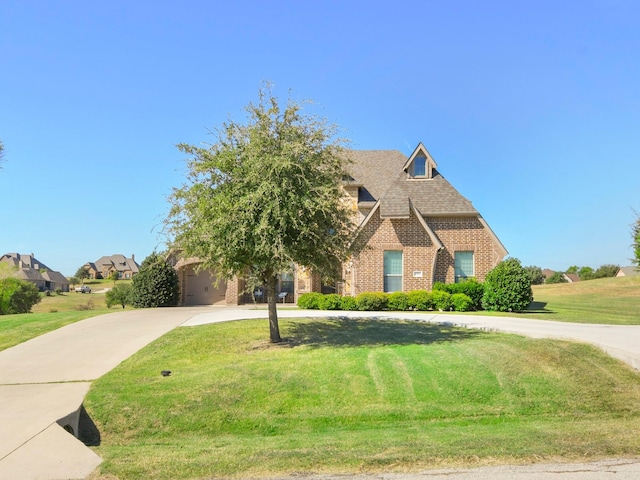 view of front of house with a front lawn, concrete driveway, brick siding, and roof with shingles