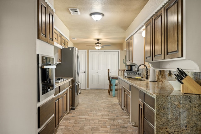 kitchen with backsplash, appliances with stainless steel finishes, a textured ceiling, light stone countertops, and sink