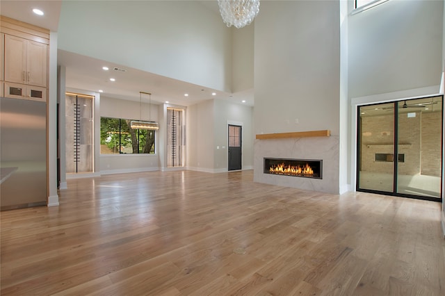 unfurnished living room with an inviting chandelier, light hardwood / wood-style flooring, and a high ceiling