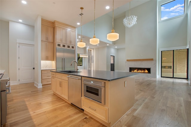 kitchen featuring stainless steel appliances, a high ceiling, pendant lighting, light brown cabinets, and a center island with sink