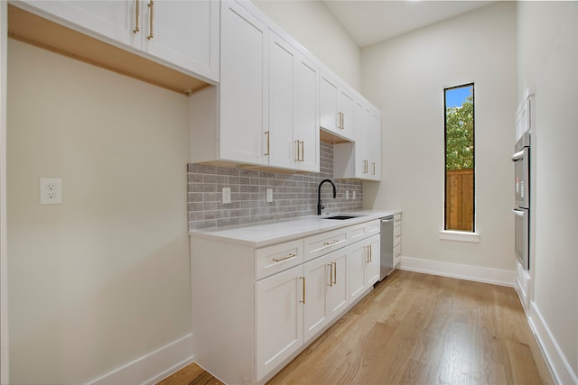 kitchen featuring tasteful backsplash, sink, stainless steel appliances, white cabinets, and light hardwood / wood-style flooring