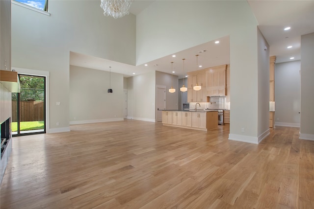 unfurnished living room with a towering ceiling, an inviting chandelier, sink, and light wood-type flooring